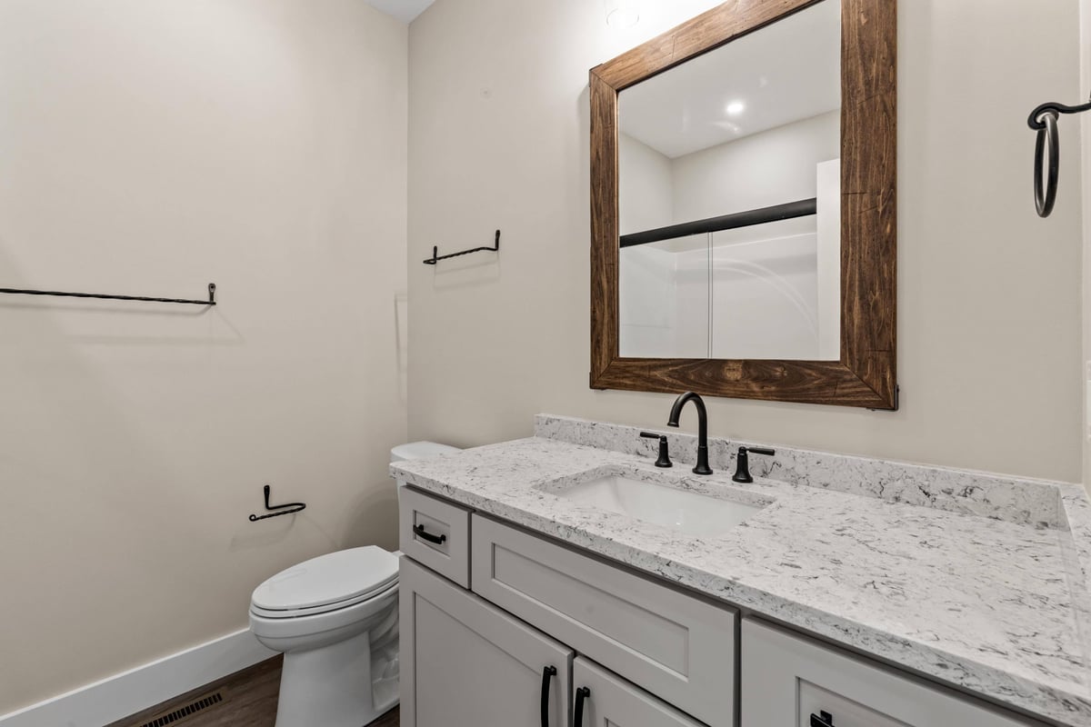 Bathroom with a quartz countertop, wood-framed mirror, and modern black fixtures in a custom home in Knoxville, TN by Debuty Builders, Inc