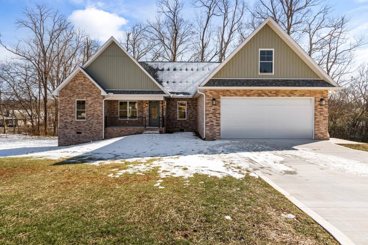 Front view of a custom brick and green siding home in Knoxville, TN by Debuty Builders, Inc., featuring a two-car garage and a snow-covered driveway