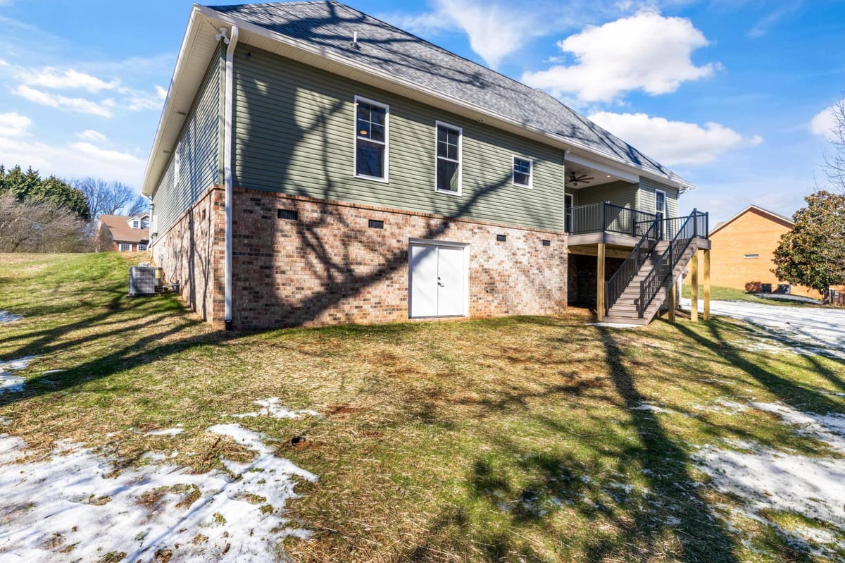 Side view of a custom home in Knoxville, TN by Debuty Builders, Inc., showcasing green siding and brick foundation with a walkout basement door