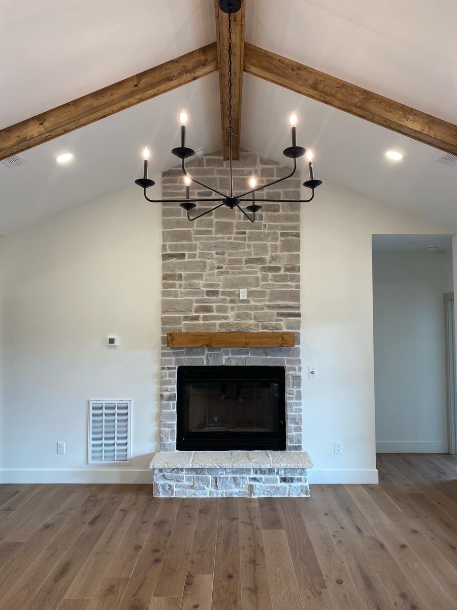 Stone fireplace with exposed wooden beams and modern chandelier in a custom home by Debuty Builders, Knoxville, TN