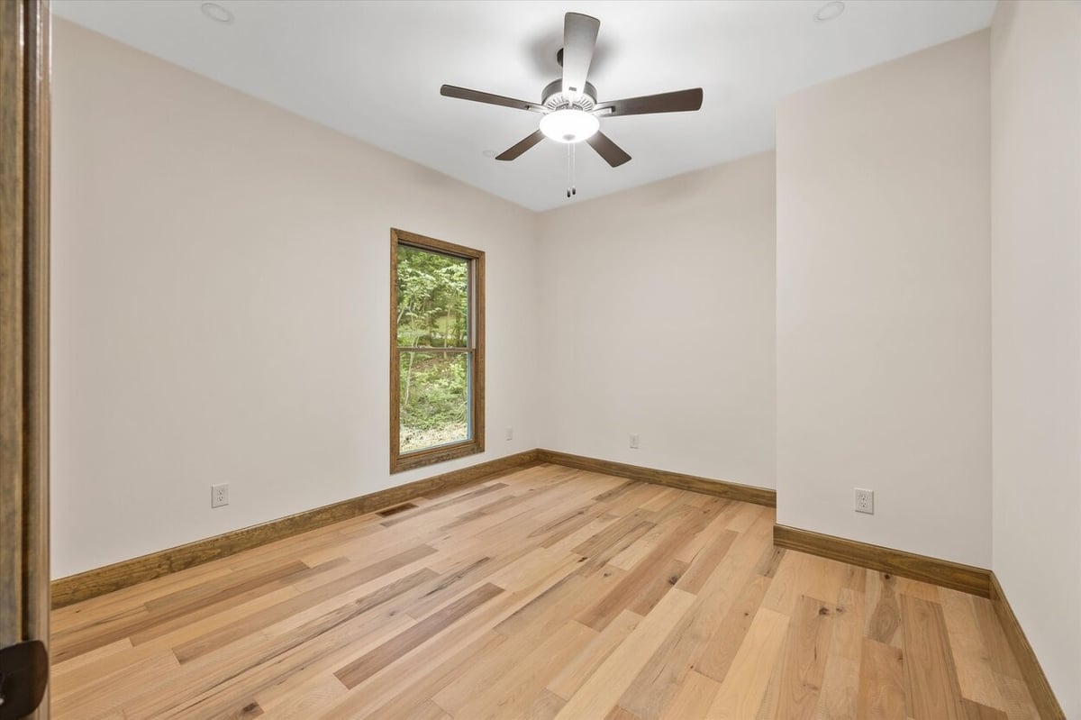 Empty bedroom with light wood floors and ceiling fan in Friendsville Custom Home in Knoxville, TN.