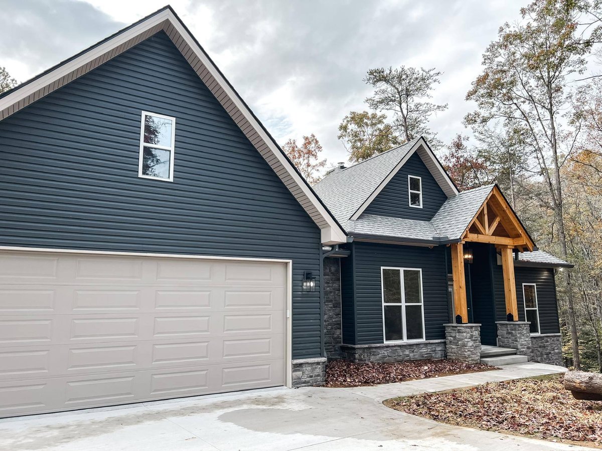 Front view of a custom home in Knoxville, TN by Debuty Builders, Inc., featuring dark siding, a timber-framed porch, and a spacious two-car garage.