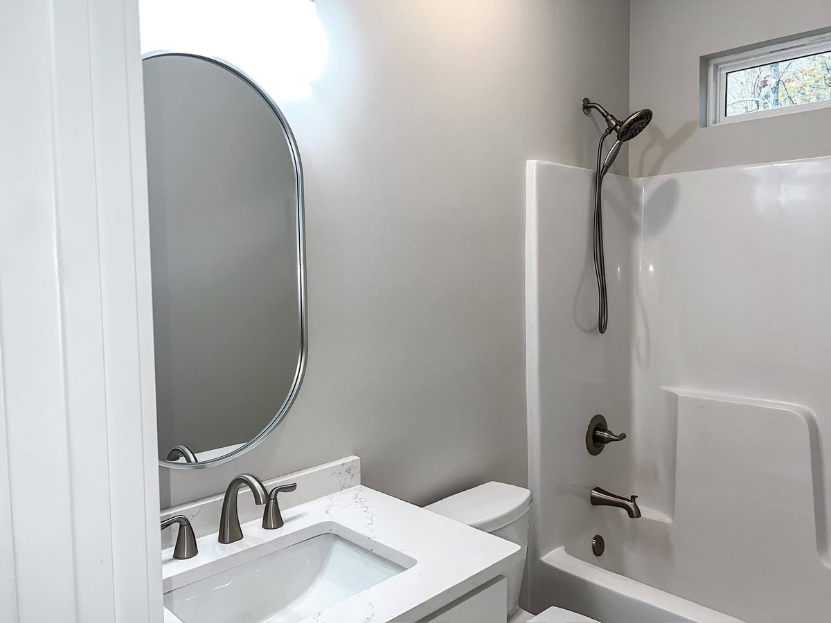 Guest bathroom featuring an oval mirror, single vanity with a white quartz countertop, and a shower-tub combination, part of a custom home in Knoxville, TN by Debuty Builders, Inc.