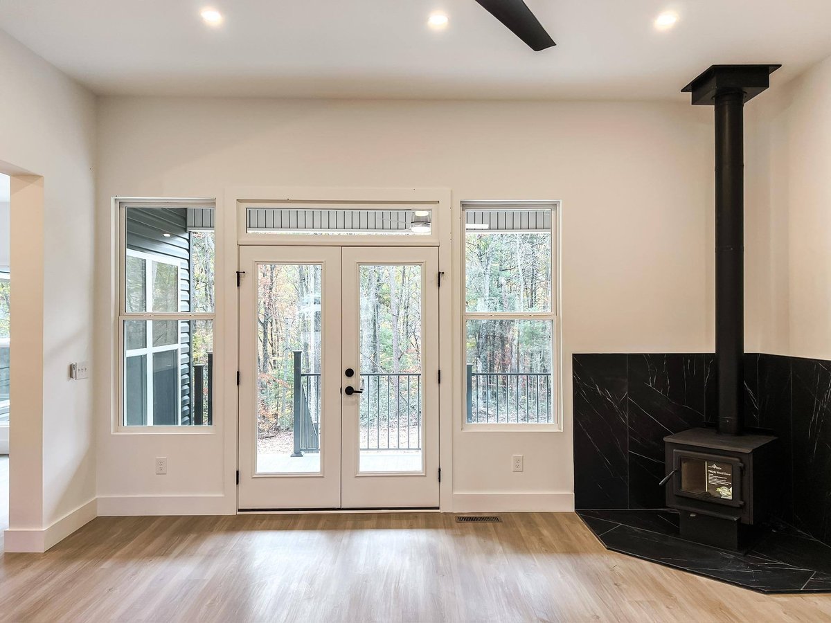 Living room featuring a black wood-burning fireplace, French doors, and views of a wooded backyard in a custom home in Knoxville, TN by Debuty Builders, Inc.