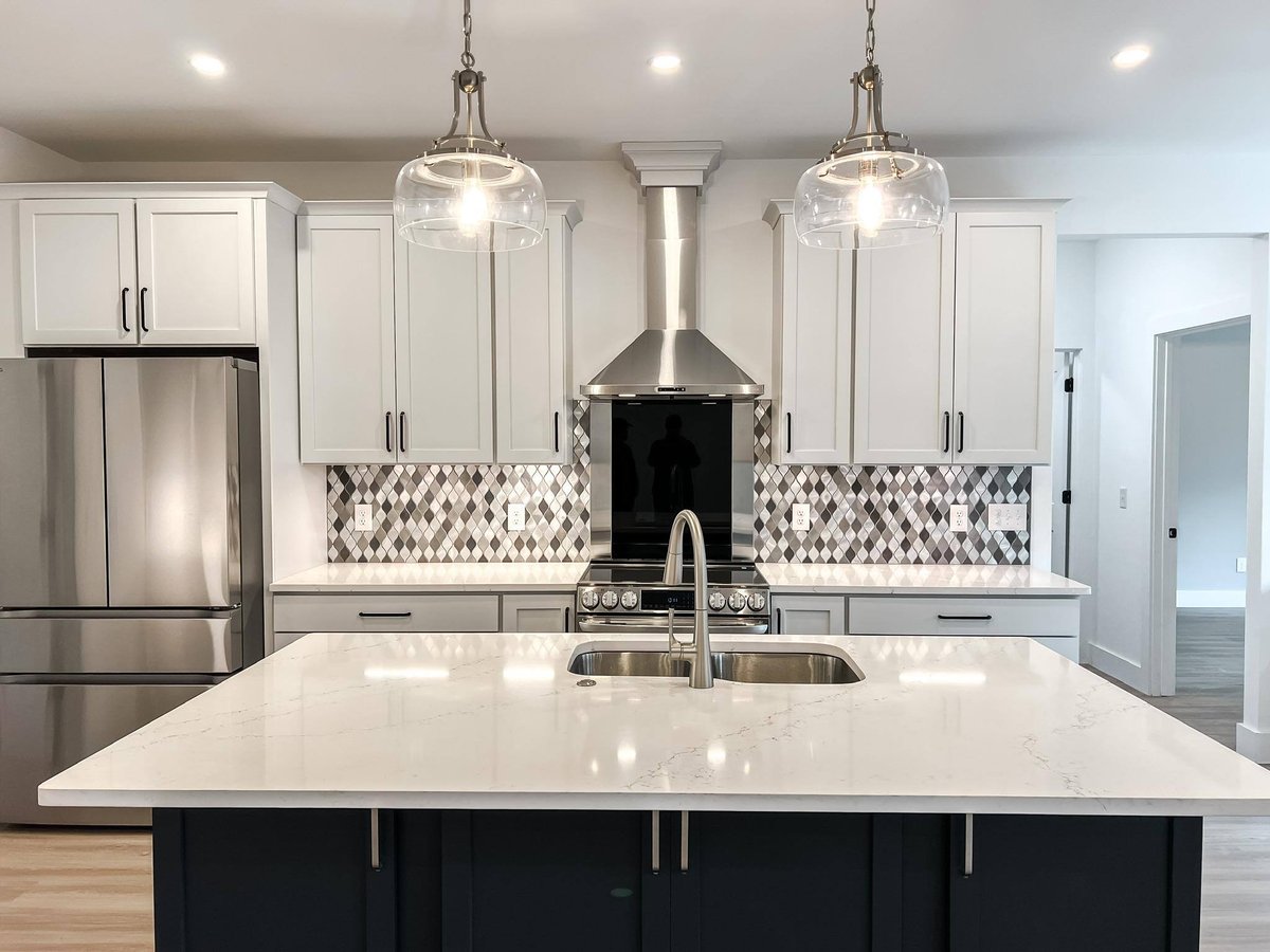 Modern kitchen featuring a large quartz island with an undermount sink, shaker cabinets, stainless steel appliances, and diamond-pattern backsplash in a custom home in Knoxville, TN by Debuty Builders, Inc