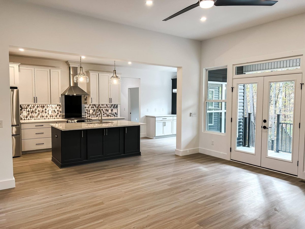 Open-concept kitchen with a modern island and glass pendant lighting, leading to a bright living area with French doors in a custom home in Knoxville, TN by Debuty Builders, Inc.