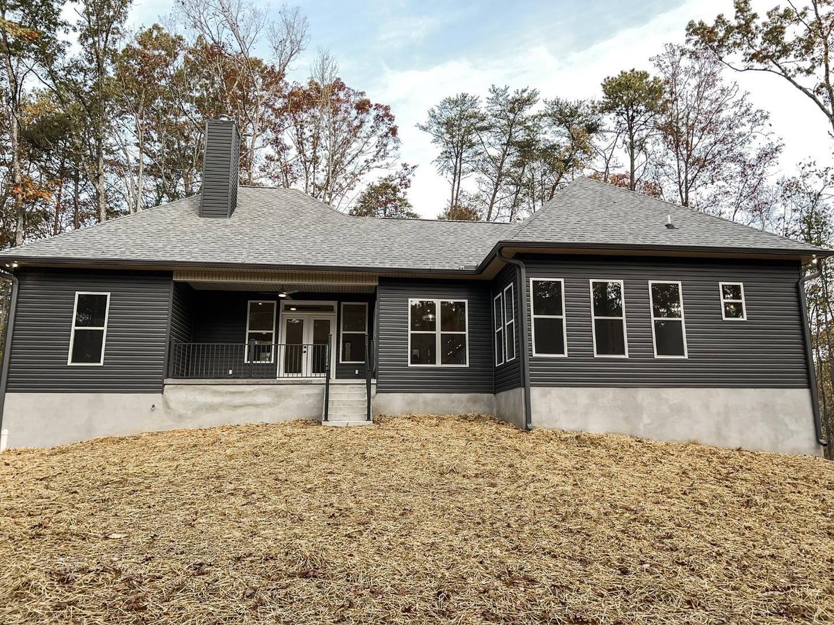 Rear view of a custom home in Knoxville, TN by Debuty Builders, Inc., featuring dark siding and a covered porch with surrounding wooded scenery.