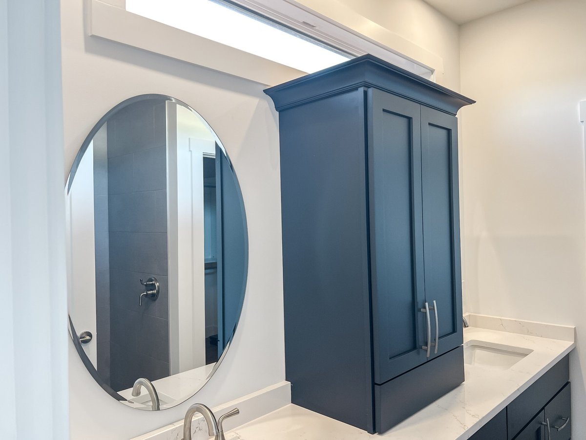 Bathroom detail in a custom home by Debuty Builders, Inc. in Maryville, TN, showing a round mirror and tall navy-blue cabinet against a white countertop