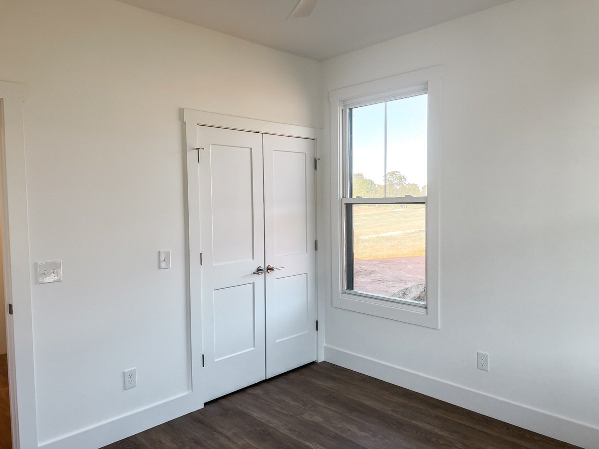 Bedroom with white double-door closet in a custom home by Debuty Builders, Inc. in Maryville, TN, featuring a single window with a view of the outdoor landscape