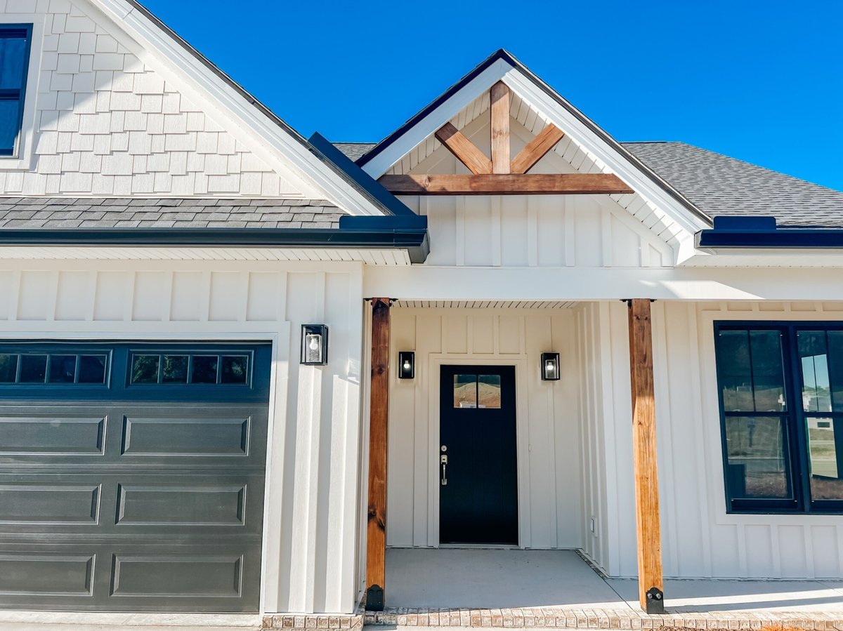 Front entry porch of a custom home by Debuty Builders, Inc. in Maryville, TN, with wood beams and board-and-batten siding around a black front door, combining rustic and modern elements