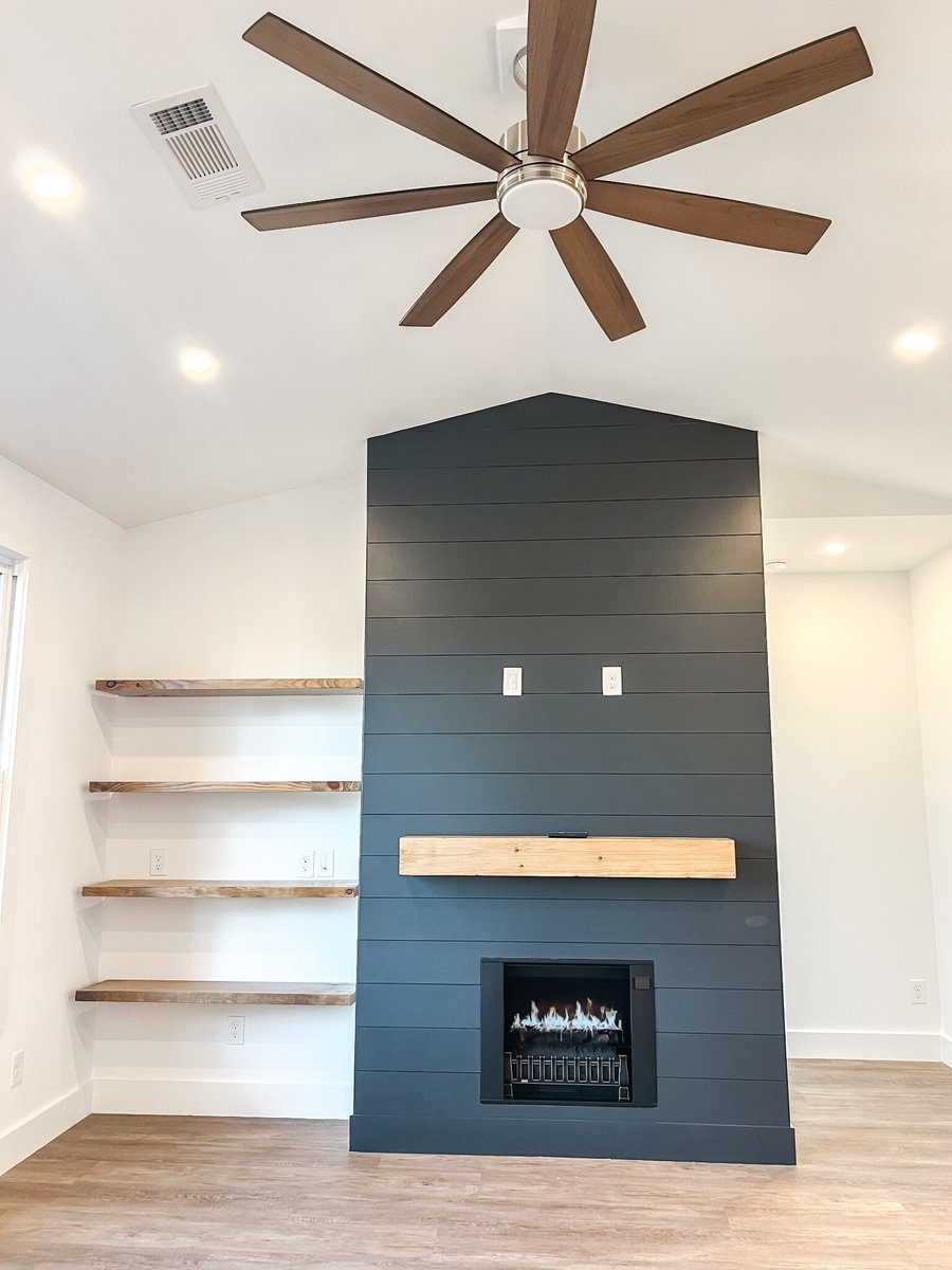 Interior of a custom home by Debuty Builders, Inc. in Maryville, TN, featuring a shiplap accent wall with a sleek black fireplace, built-in shelving, and a large modern ceiling fan.