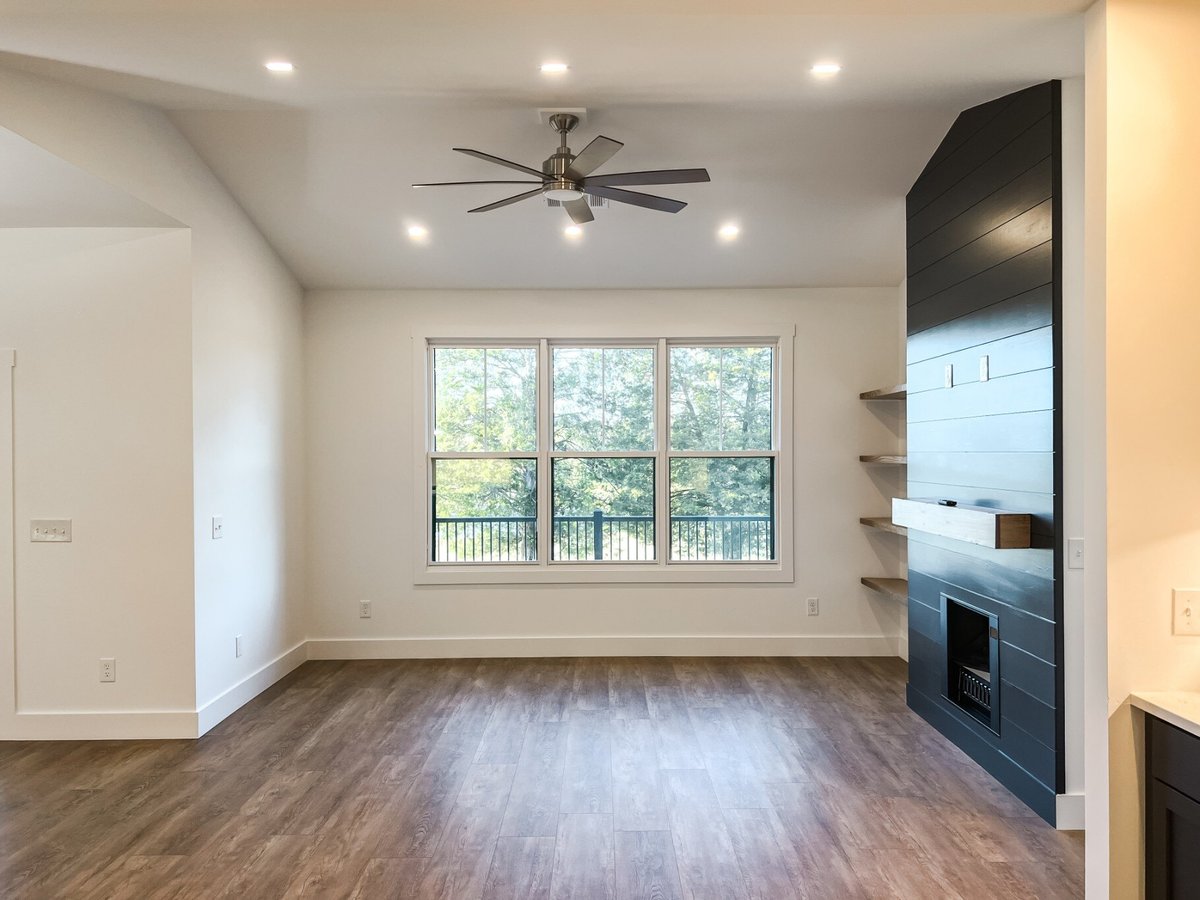 Spacious living room in a custom home by Debuty Builders, Inc. in Maryville, TN, with large windows providing ample natural light, an accent wall with a fireplace, and wooden flooring